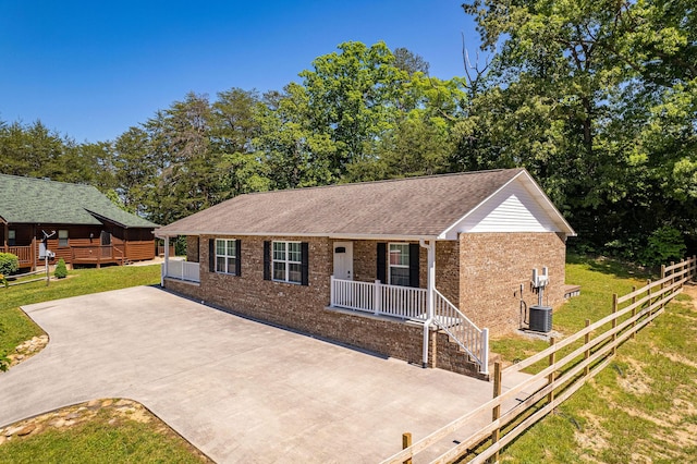 single story home with a porch, brick siding, central AC, fence, and a front lawn