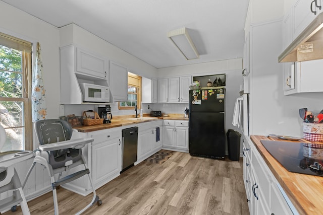 kitchen featuring under cabinet range hood, a wealth of natural light, white cabinets, black appliances, and wood counters