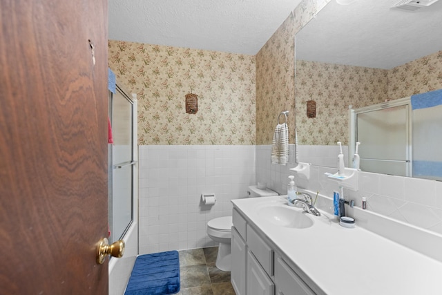 full bathroom featuring a textured ceiling, toilet, wainscoting, and wallpapered walls