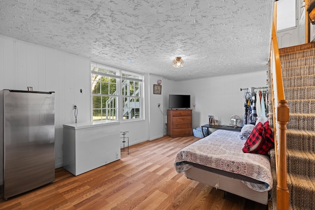 bedroom featuring stainless steel refrigerator, a textured ceiling, light wood-type flooring, and fridge