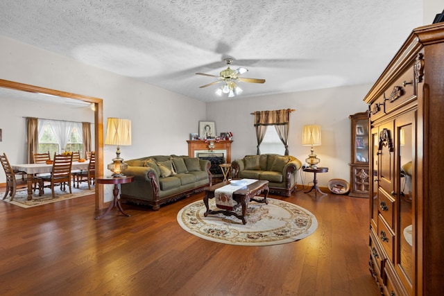 living room featuring ceiling fan, a textured ceiling, and dark wood-type flooring