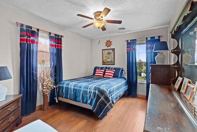 bedroom with multiple windows, ceiling fan, hardwood / wood-style floors, and a textured ceiling