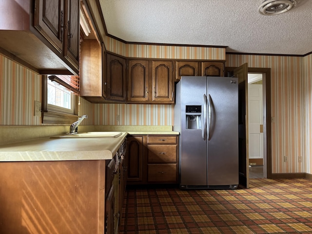 kitchen featuring a sink, a textured ceiling, stainless steel fridge, wallpapered walls, and light countertops