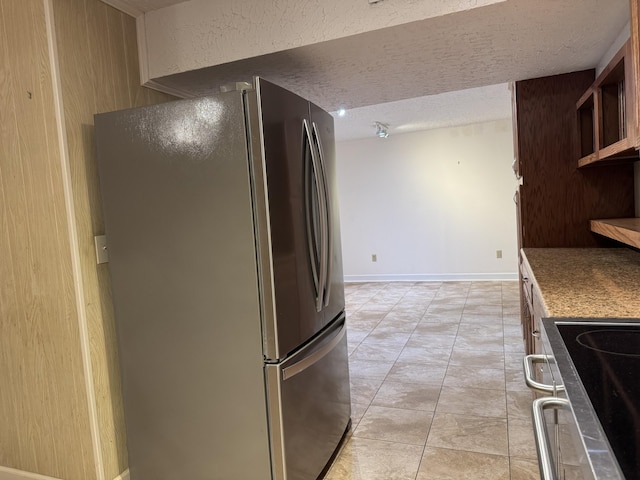 kitchen with baseboards, light tile patterned floors, freestanding refrigerator, a textured ceiling, and range