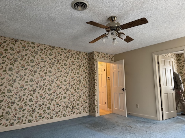 empty room featuring visible vents, a textured ceiling, carpet, wallpapered walls, and ceiling fan