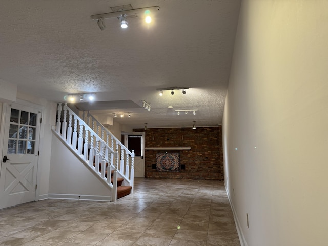 interior space with a textured ceiling, brick wall, rail lighting, baseboards, and stairs