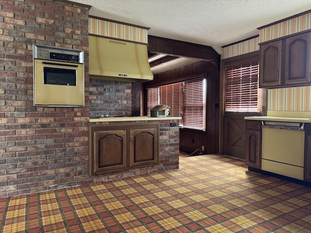 kitchen featuring dishwashing machine, oven, light countertops, a textured ceiling, and exhaust hood