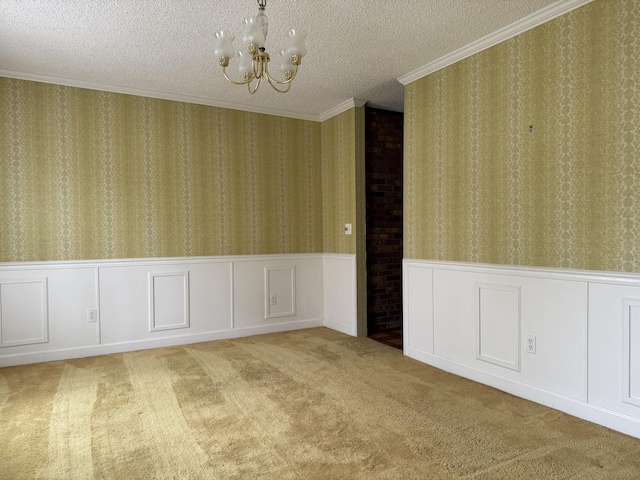 carpeted empty room featuring a textured ceiling, wallpapered walls, ornamental molding, wainscoting, and a notable chandelier