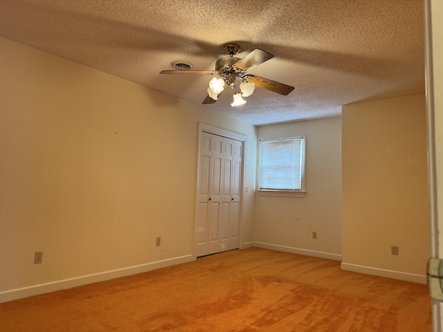 unfurnished bedroom featuring baseboards, light carpet, a closet, a textured ceiling, and a ceiling fan