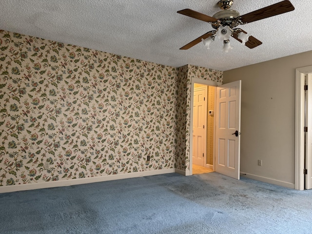 unfurnished room featuring a textured ceiling, carpet flooring, wallpapered walls, baseboards, and ceiling fan