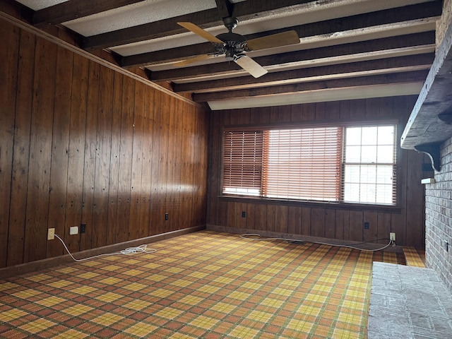 spare room featuring beam ceiling, wooden walls, and ceiling fan