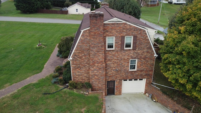 view of side of property with a yard, concrete driveway, an attached garage, brick siding, and a chimney