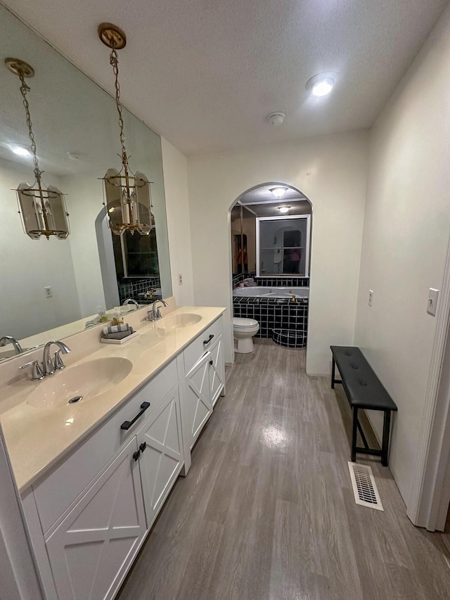 bathroom with a bathtub, vanity, a textured ceiling, wood-type flooring, and toilet