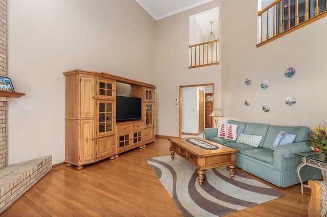 living room featuring a fireplace, a towering ceiling, baseboards, light wood finished floors, and crown molding