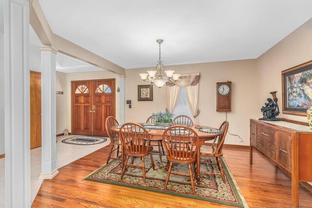 dining area featuring a notable chandelier, decorative columns, baseboards, and wood finished floors