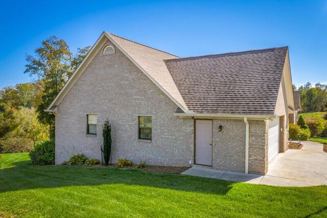 exterior space with concrete driveway, a shingled roof, a front yard, and brick siding