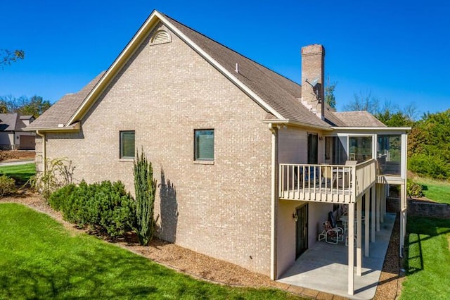 back of house with a sunroom, a chimney, a yard, a patio area, and brick siding