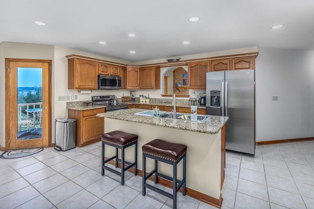 kitchen with brown cabinets, a kitchen island with sink, stainless steel appliances, a sink, and light tile patterned flooring