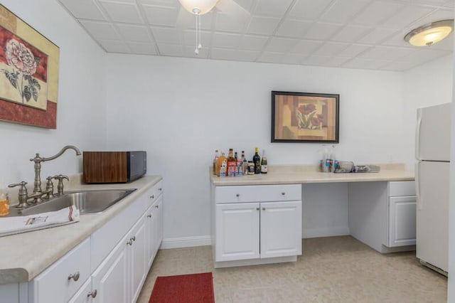 kitchen with a sink, baseboards, white cabinets, light countertops, and freestanding refrigerator