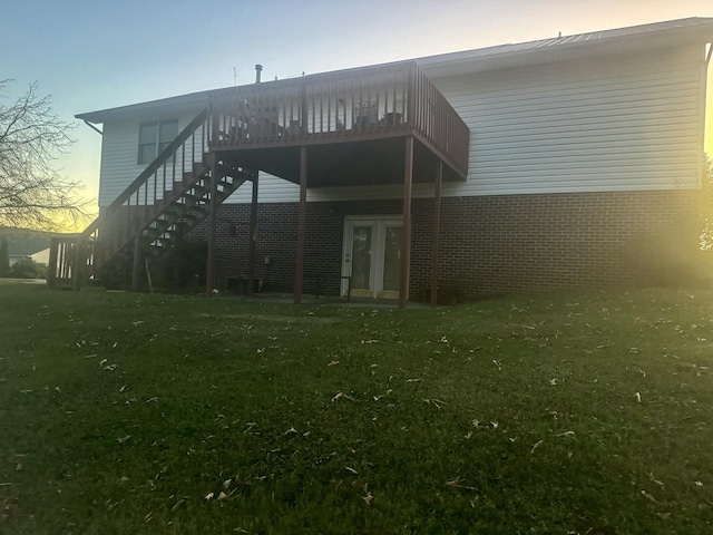 back house at dusk featuring a lawn and a deck