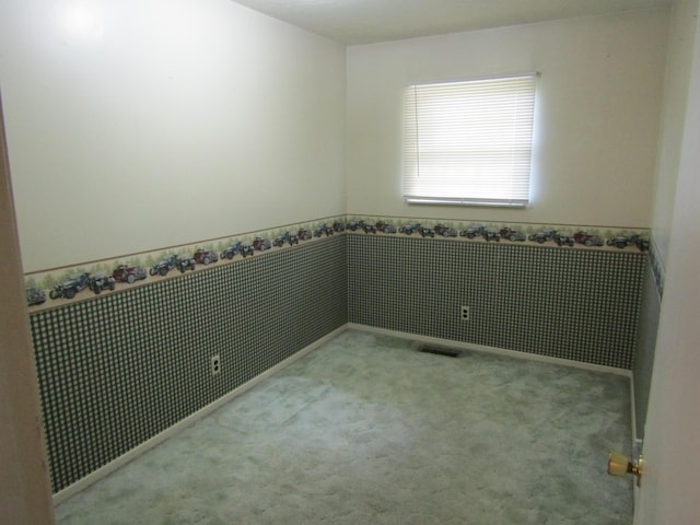 carpeted empty room featuring visible vents and a wainscoted wall