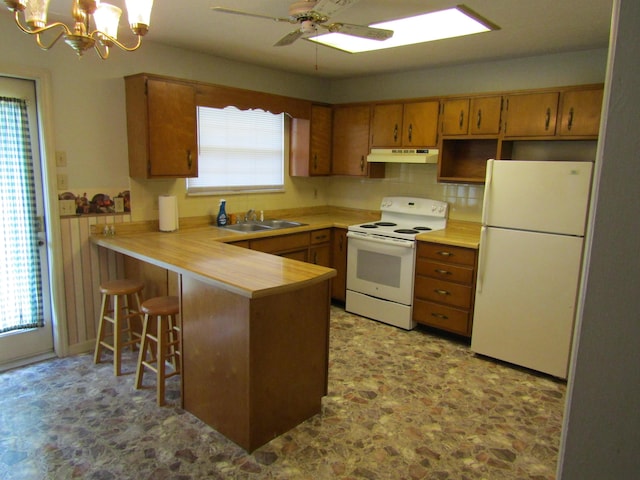 kitchen with a peninsula, a sink, white appliances, light countertops, and under cabinet range hood