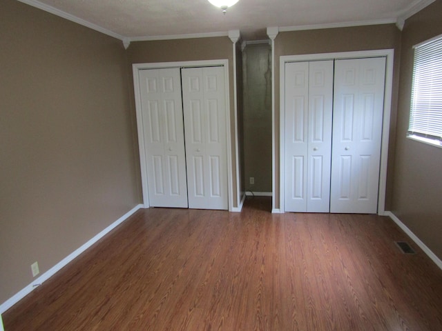 unfurnished bedroom with visible vents, baseboards, multiple closets, and wood finished floors