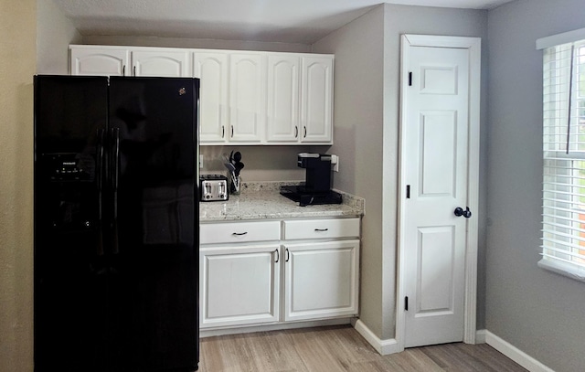 kitchen with light stone countertops, light wood-type flooring, white cabinetry, and black fridge