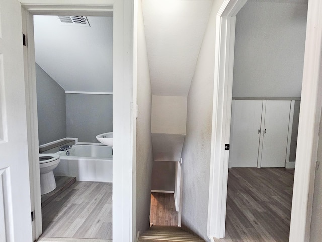 bathroom featuring hardwood / wood-style floors, vaulted ceiling, toilet, and a bathing tub