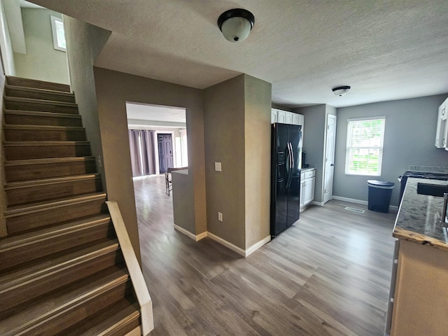 kitchen with wood-type flooring, a textured ceiling, white cabinetry, and black fridge