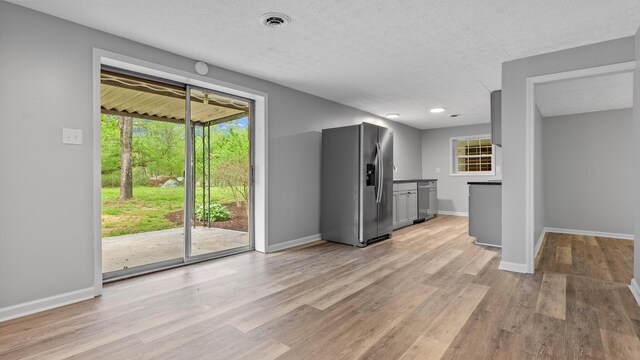 kitchen with light wood finished floors, a textured ceiling, stainless steel appliances, baseboards, and visible vents
