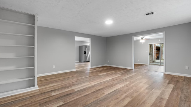 unfurnished room with built in features, ceiling fan, a textured ceiling, and wood finished floors