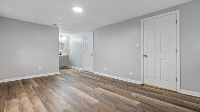 unfurnished bedroom with baseboards, ensuite bathroom, a textured ceiling, and wood finished floors