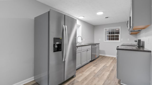 kitchen with dark countertops, baseboards, light wood-type flooring, a sink, and stainless steel appliances