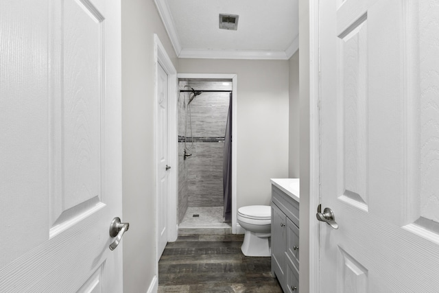 bathroom with hardwood / wood-style flooring, tiled shower, vanity, ornamental molding, and toilet