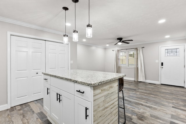 kitchen featuring a center island, light stone counters, white cabinets, a kitchen bar, and decorative light fixtures