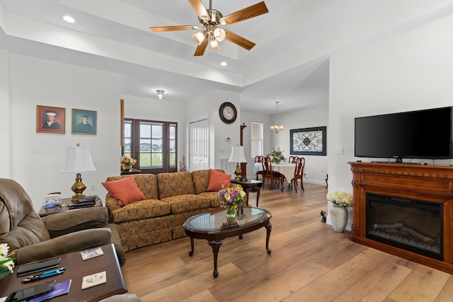 living room with a raised ceiling, light hardwood / wood-style floors, and ceiling fan with notable chandelier