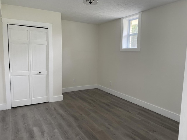 unfurnished bedroom featuring a closet, baseboards, dark wood-type flooring, and a textured ceiling