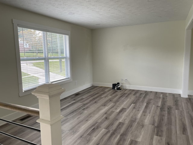 unfurnished room featuring a wealth of natural light, baseboards, a textured ceiling, and light wood finished floors