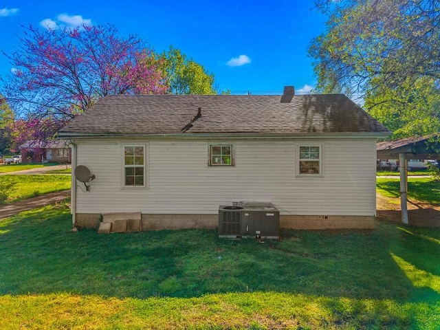 rear view of property featuring central AC unit, a yard, and a shingled roof