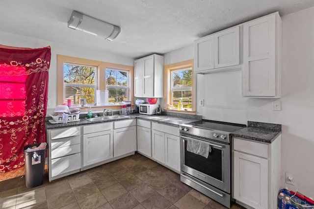 kitchen featuring dark countertops, a sink, a textured ceiling, stainless steel range with electric stovetop, and white cabinetry