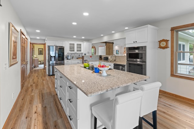 kitchen with a kitchen island, appliances with stainless steel finishes, white cabinets, and light wood finished floors