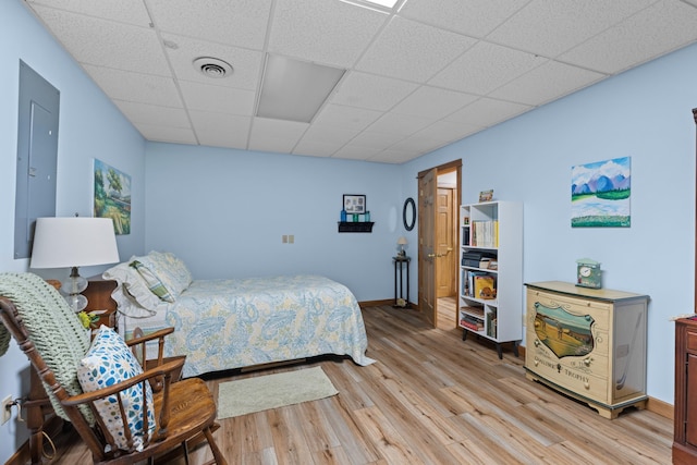 bedroom with a drop ceiling, visible vents, baseboards, and light wood-style flooring