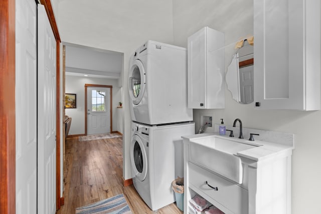 clothes washing area with light wood-type flooring, stacked washer and dryer, a sink, cabinet space, and baseboards