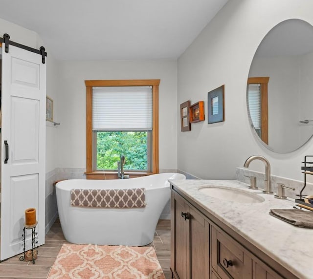 bathroom with a freestanding tub, a wainscoted wall, wood finished floors, tile walls, and vanity