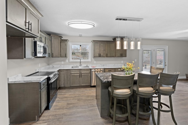 kitchen featuring sink, hardwood / wood-style flooring, appliances with stainless steel finishes, hanging light fixtures, and a center island