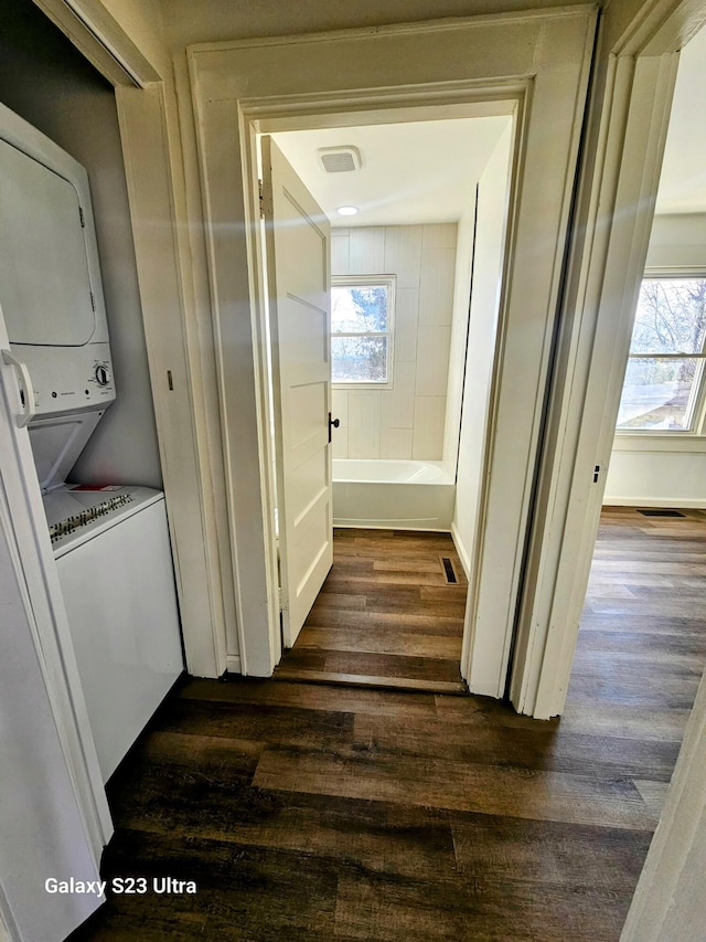 clothes washing area with stacked washing maching and dryer, dark hardwood / wood-style floors, and a healthy amount of sunlight