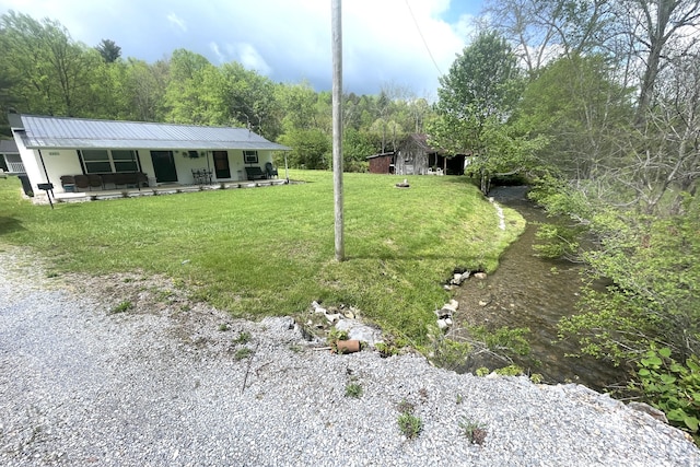 view of yard featuring covered porch and a view of trees