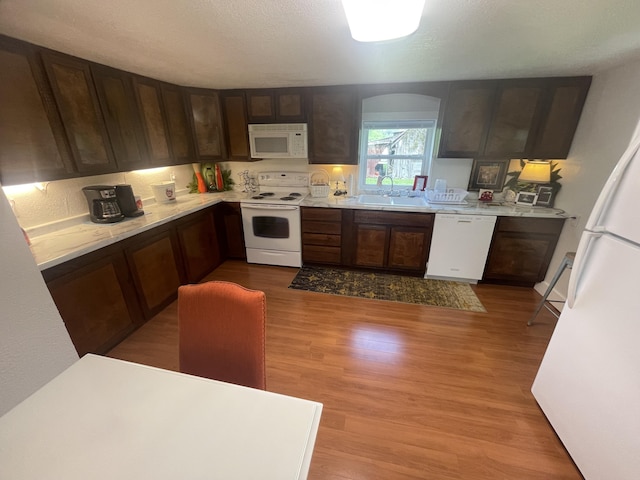 kitchen with a sink, wood finished floors, white appliances, light countertops, and arched walkways