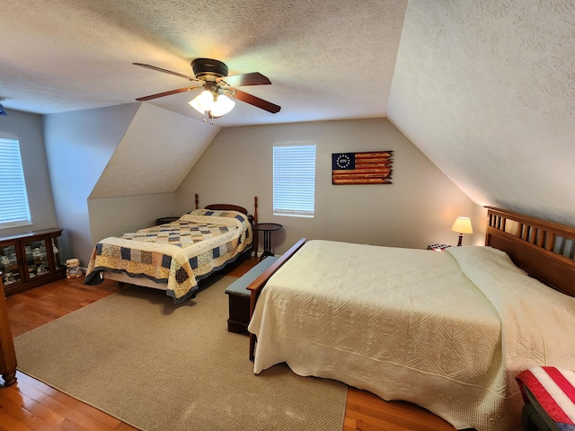 bedroom featuring lofted ceiling, a textured ceiling, a ceiling fan, and wood finished floors